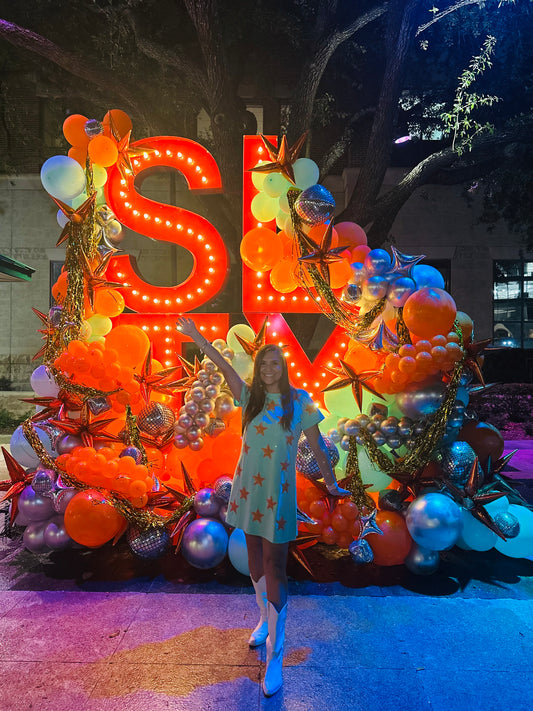 Woman posing in front of a large, colorful sugar land  sign with balloons and decorations.